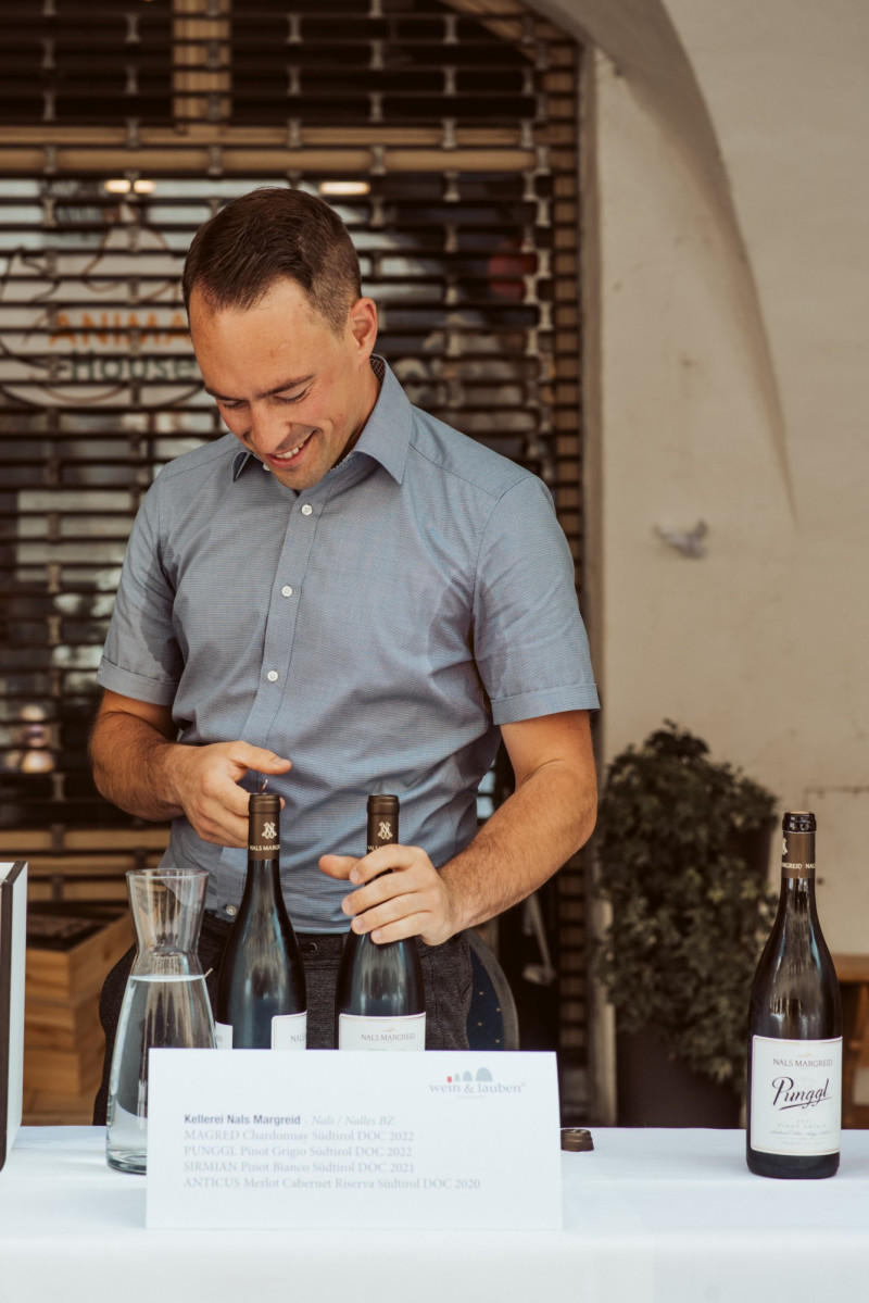 Mann öffnet Weinflasche - Wein&Lauben