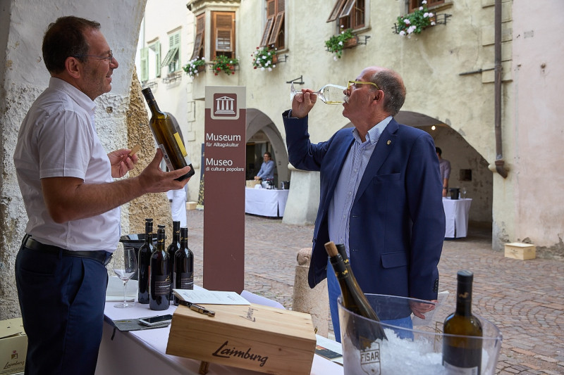 Weinhändler im Gespräch mit einem Passanten, der seinen Wein kostet - Wein&Lauben