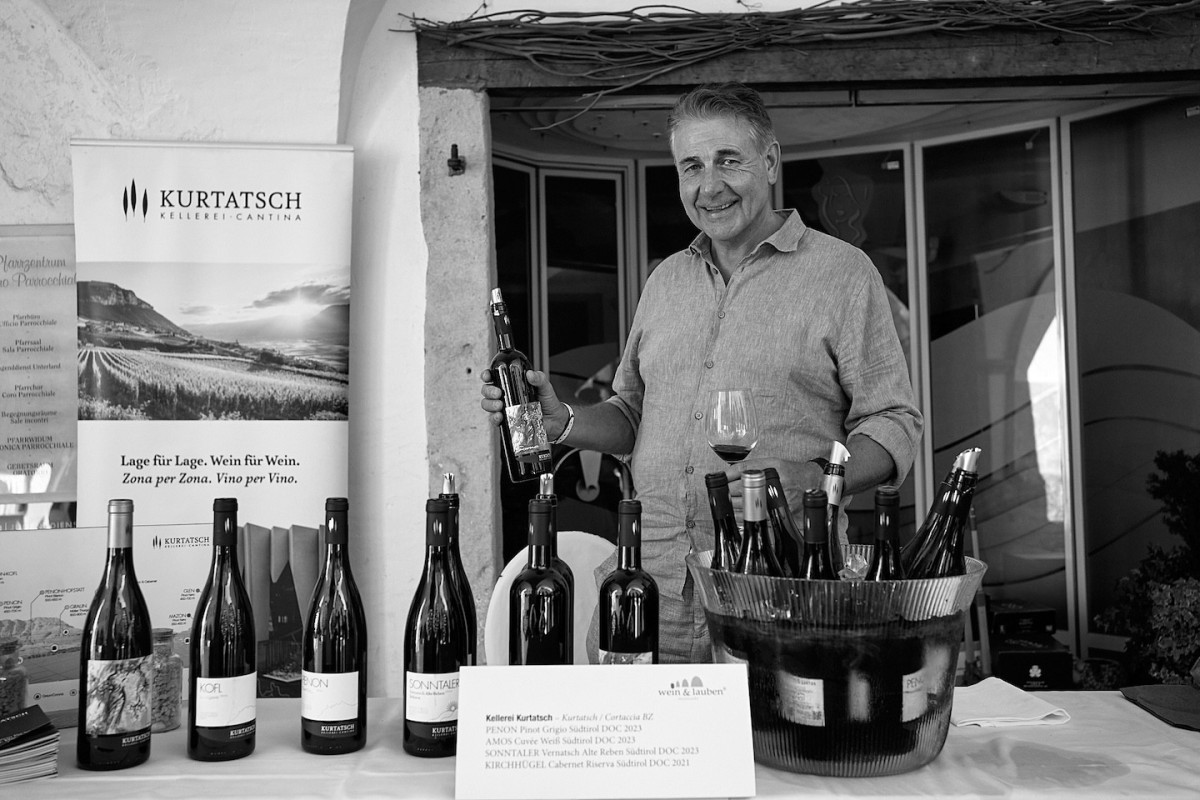 Ein Vertreter von Kellerei Kurtatsch steht mit einer Besucherin am Stand und verkostet Wein.