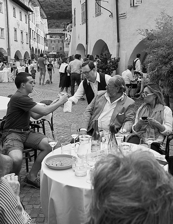 Gäste des Wein&Lauben Festes bei Trank und Speis, während Vincenzo ein Getränk reicht